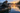 Angler lowering a portable fish finder transducer beside a kayak at sunrise